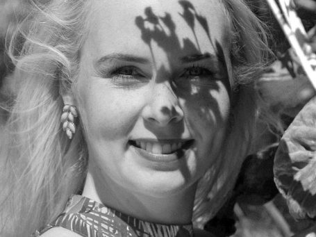 Junge Frau mit blondem Haar in floraler Umgebung mit Licht und Schatten.